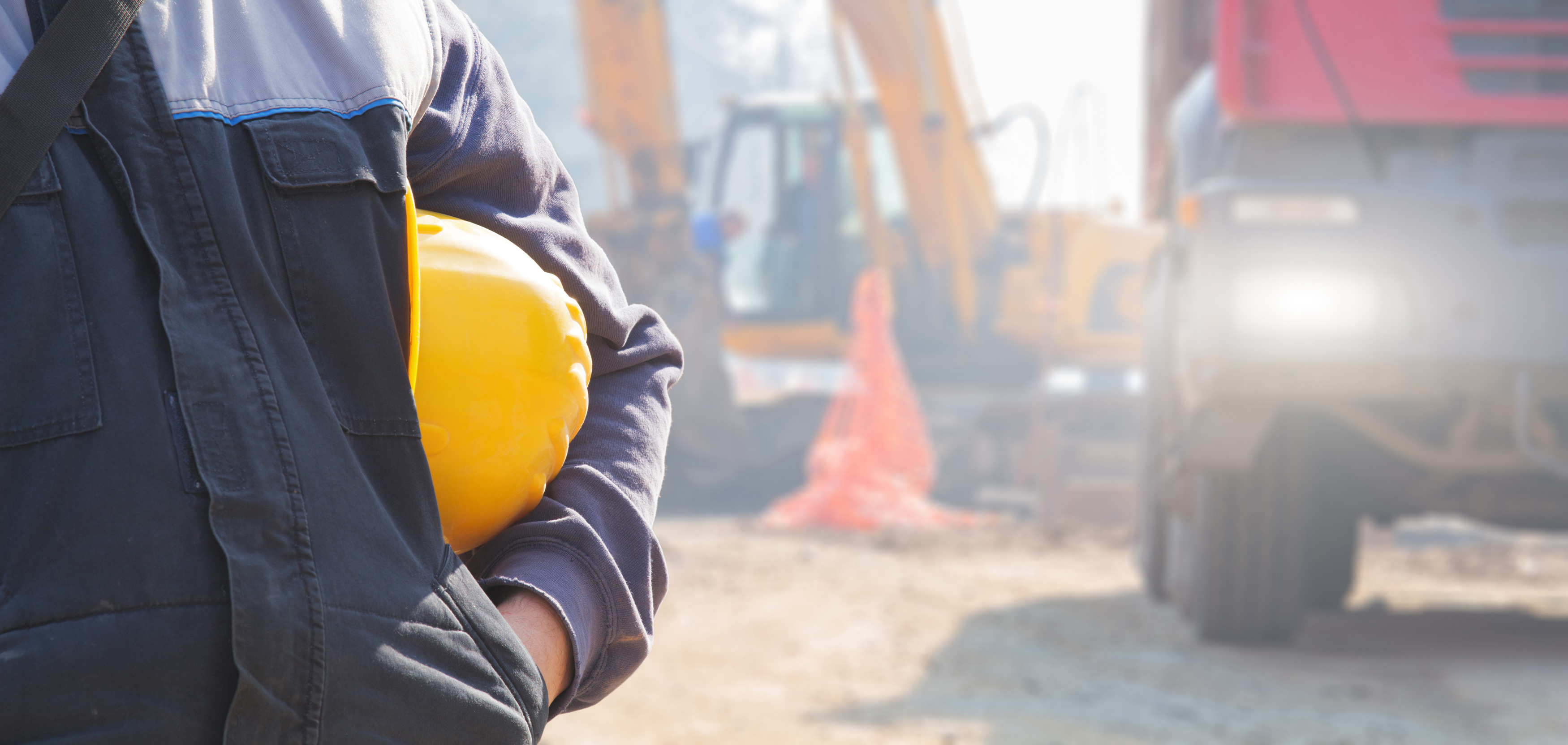 Construction professional holding a yellow hard hat at a worksite